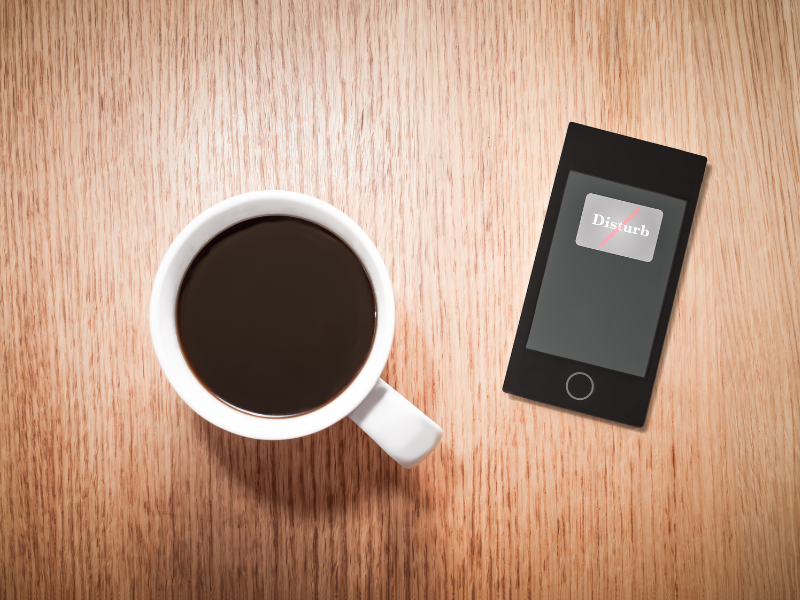 A cup of coffee next toa phone with "do not disturb" on the screen