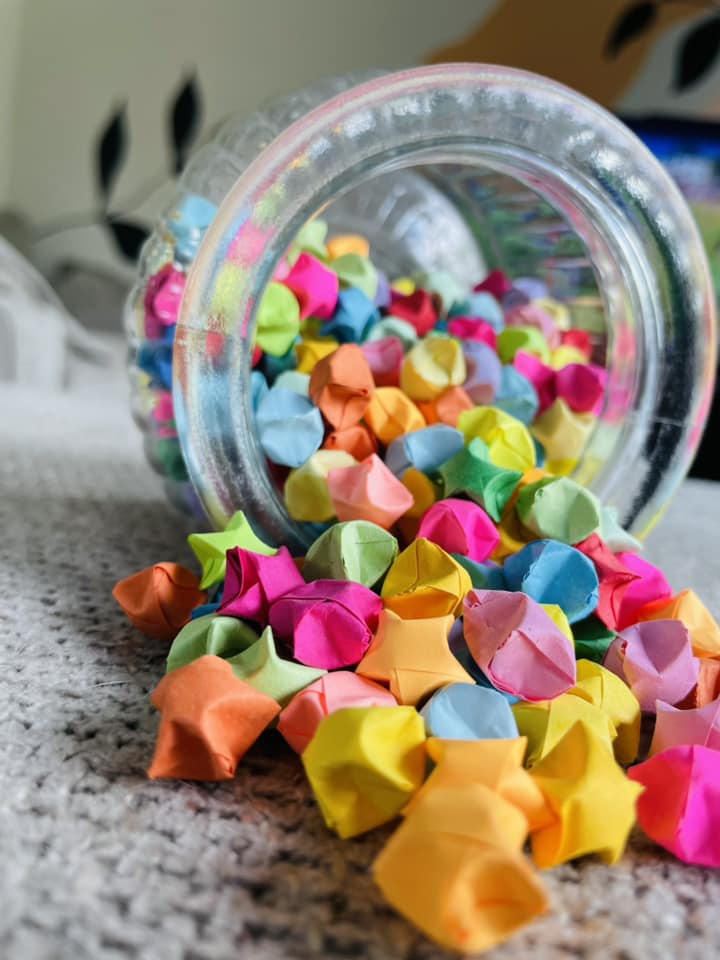 An open jar lays on it's side on carpet, with bright, colourful origami stars tumbling out