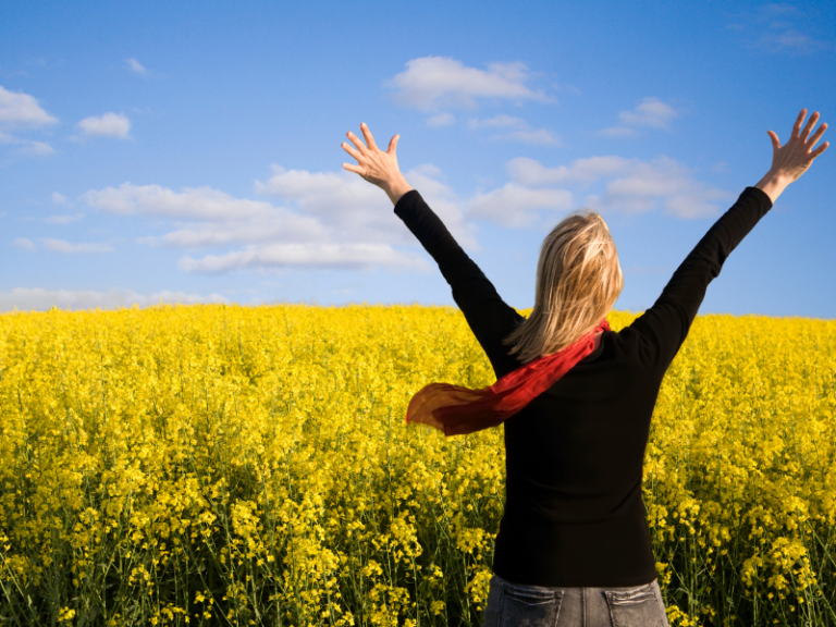 A woman raises her srms in celebration, surrounded by wheat plants