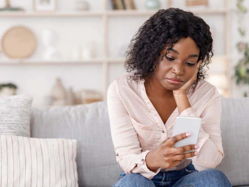 A woman looks disappointed as she looks at her mobile phone.